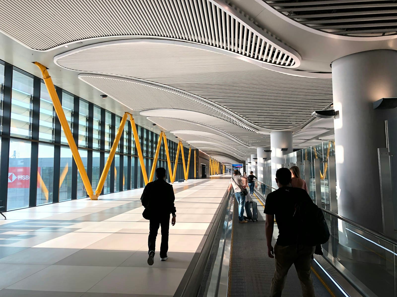 Reizigers lopen door een lichte terminal met warme gele accenten